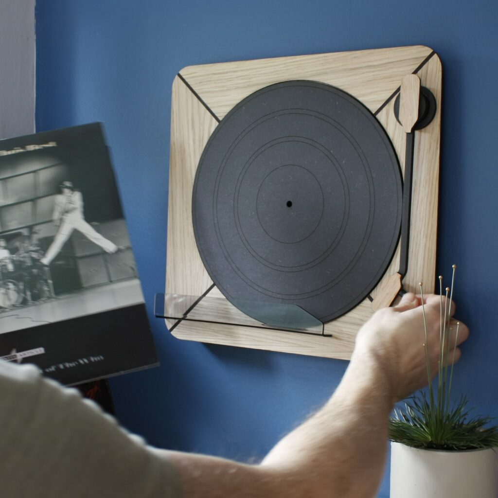 Vinyl record sleeve shown being placed onto the Exposure vinyl record display with someone about to rotate the arm around to hold the vinyl sleeve in place.
