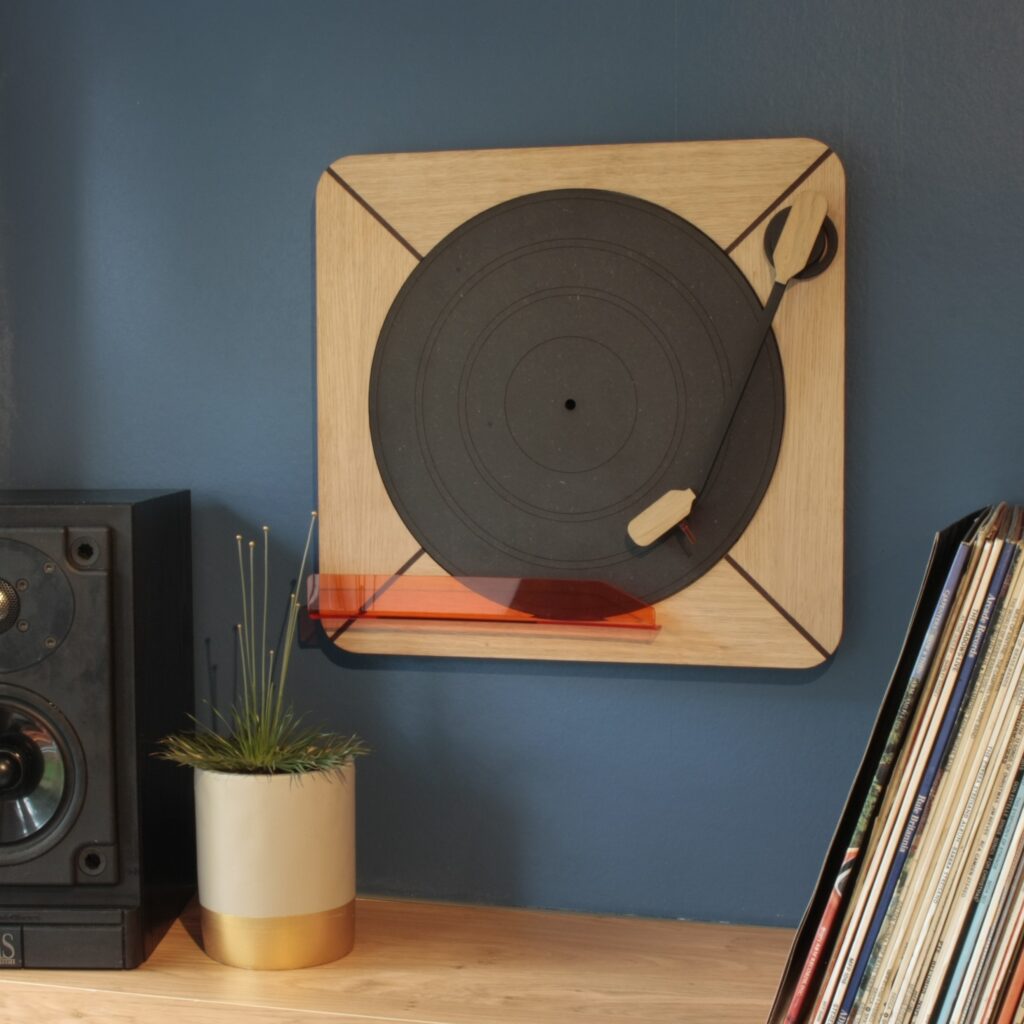 Exposure vinyl record holder shown hanging on the wall above a shelf with a speaker, a plant and some vinyl records.